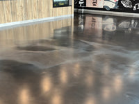 Thumbnail for Metallic epoxy garage floor with a smooth satin AQUALAB urethane topcoat reflecting honeycomb hex lighting and modern wall graphics.