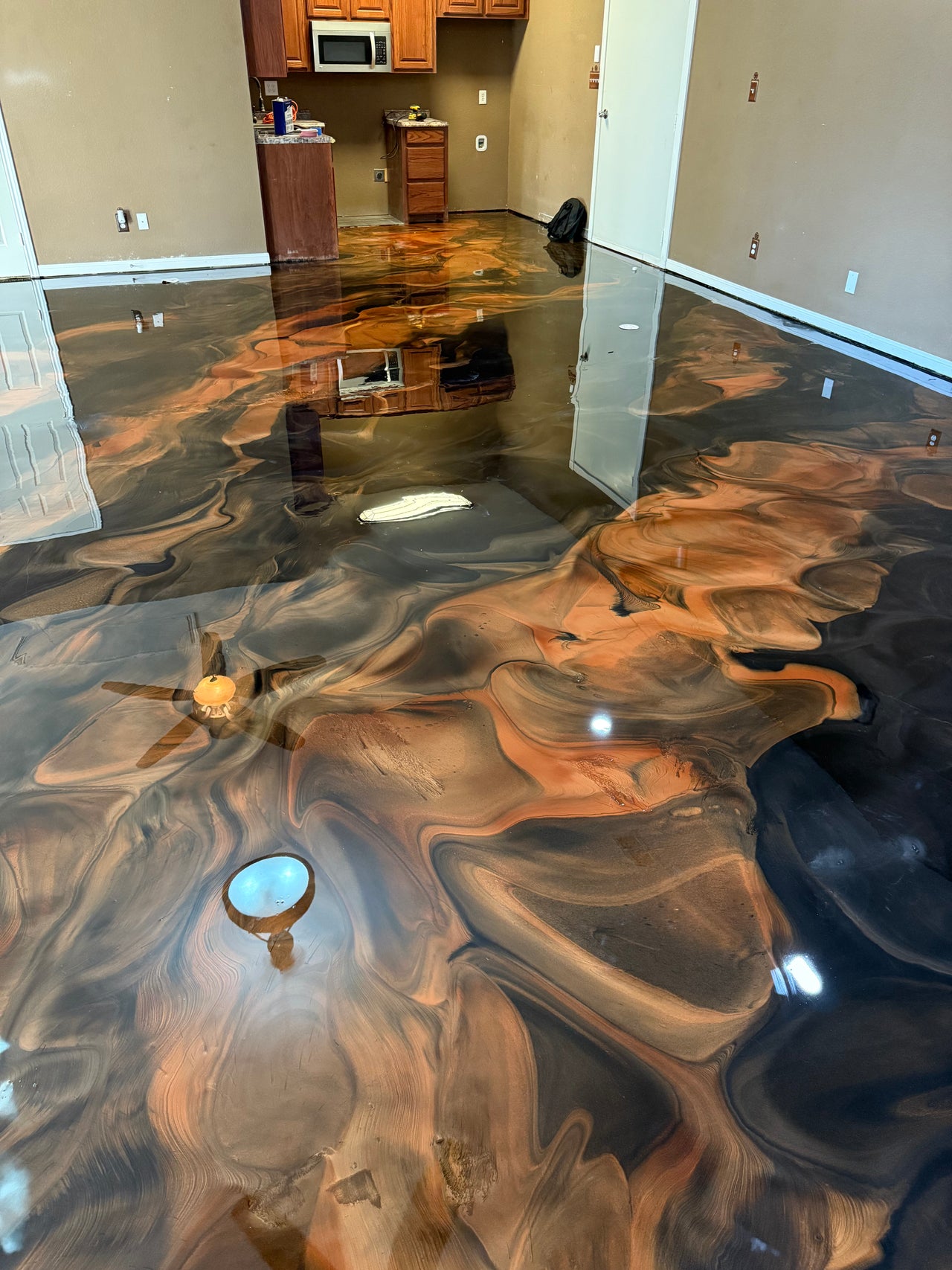 Seamless metallic epoxy kitchen floor featuring a high-gloss Black Bronze swirling marble effect with a scratch-resistant Premera T2 MCM topcoat.