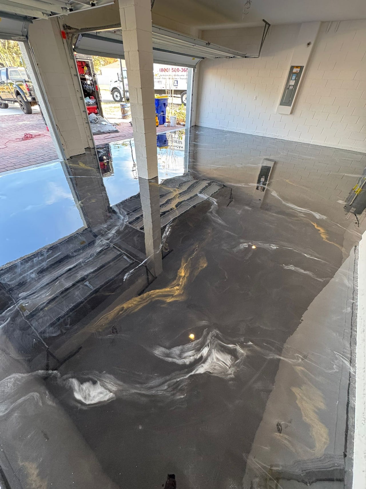 Luxury garage floor featuring a black, gold, and white metallic epoxy marble design with a high-gloss, showroom-quality finish.
