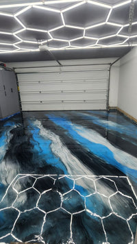 Thumbnail for Modern garage showroom with a blue, black, and white metallic epoxy floor and overhead honeycomb hex lighting for a high-gloss, reflective finish.