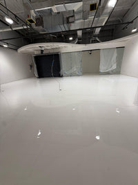 Thumbnail for Large commercial showroom under construction featuring a high-gloss white metallic epoxy floor with a seamless finish