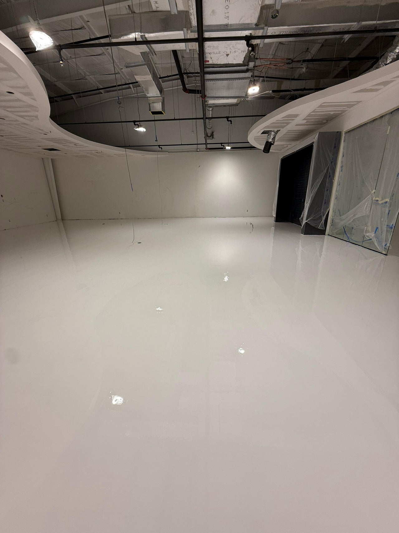 Large empty warehouse with a high-gloss white epoxy floor and industrial ceiling