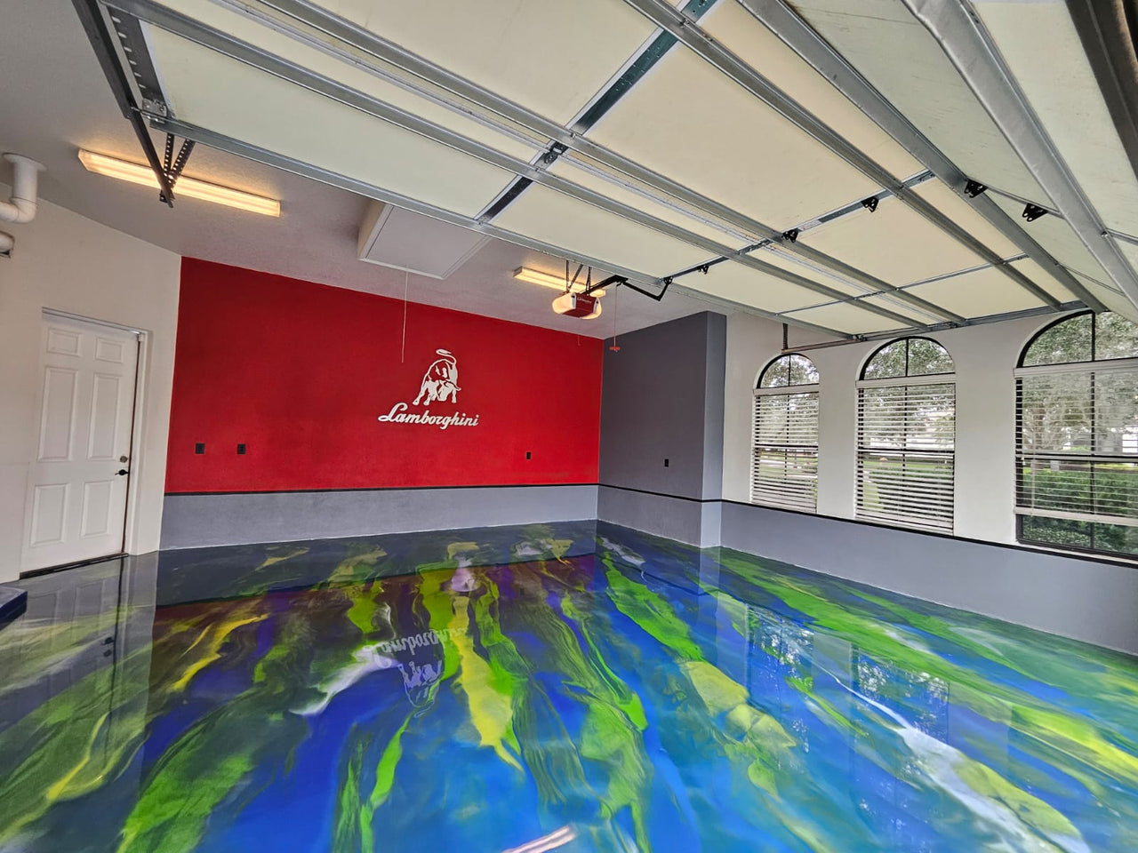 Luxury garage showroom featuring a vibrant blue, green, and yellow metallic epoxy floor with dynamic 3D marbling and a high-gloss finish, themed for Lamborghini supercars.